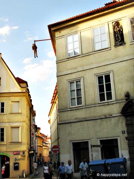 photo of a building with a statue of a man hanging by a rod extending from its rooftop, at the Old Town in Prague