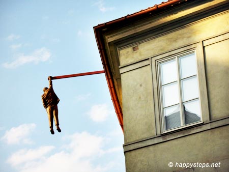 photo of a building with a statue of a man hanging by a rod extending from its rooftop, at the Old Town in Prague